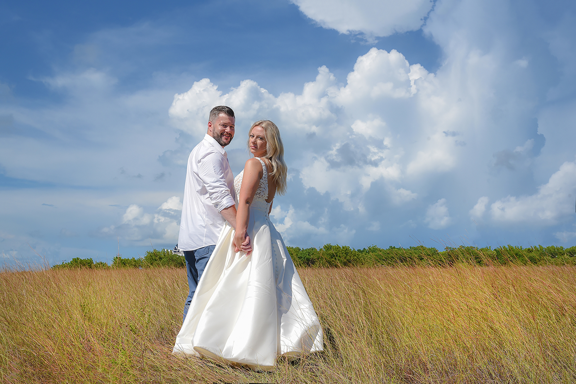 Wedding couple holding hands in a grassy field